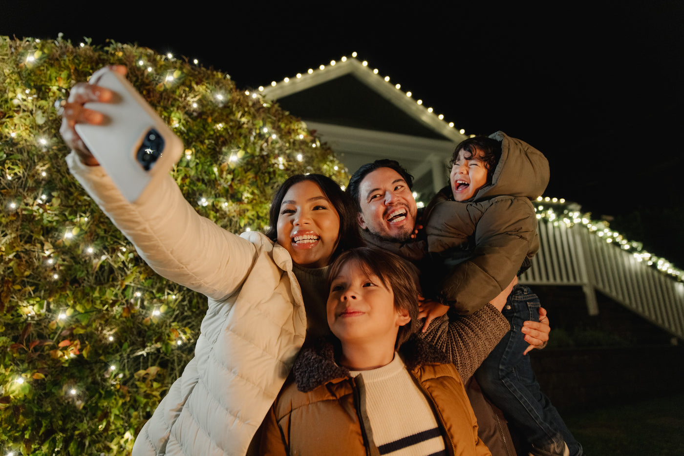 Family taking a selfie in front of a decorated Christmas house.